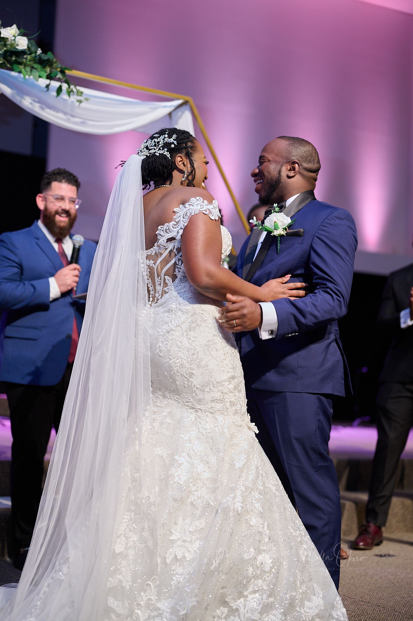 Close-up of wedding ceremony with couple and officiant sharing a joyful moment under draped arch.