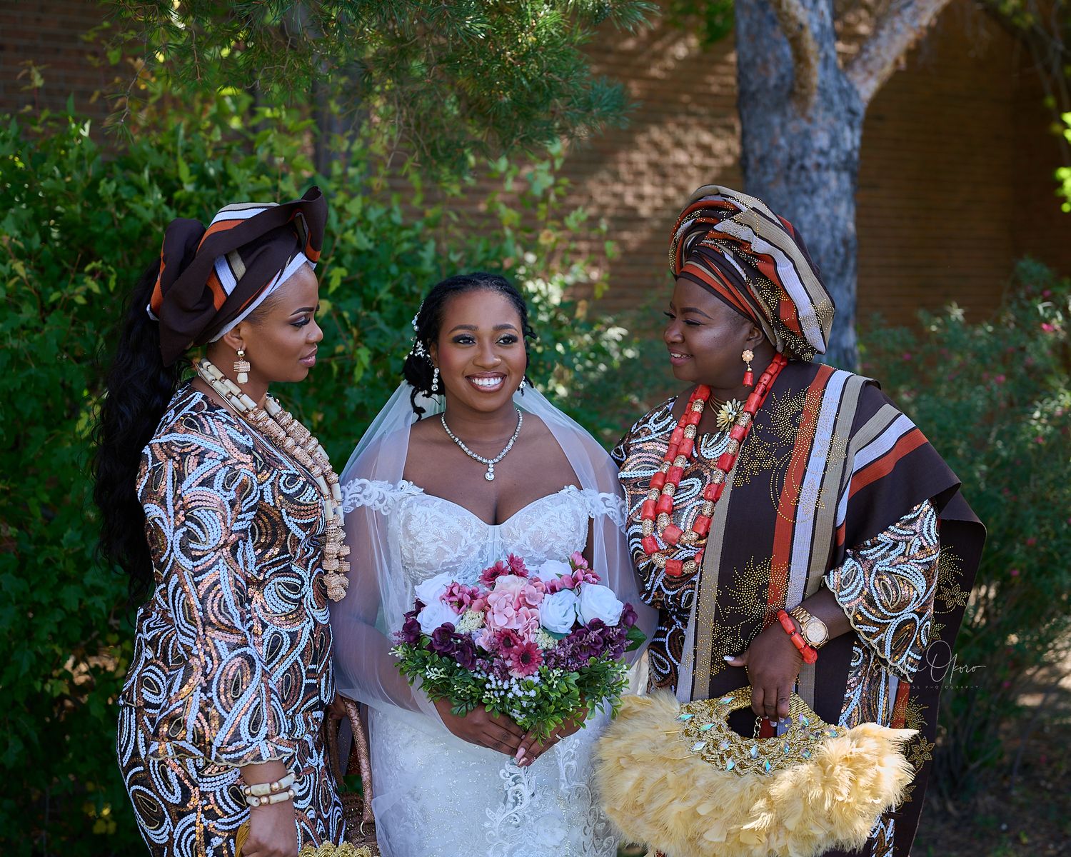 Beautiful traditional African wedding attire with colorful prints and elaborate headdresses at an outdoor ceremony.