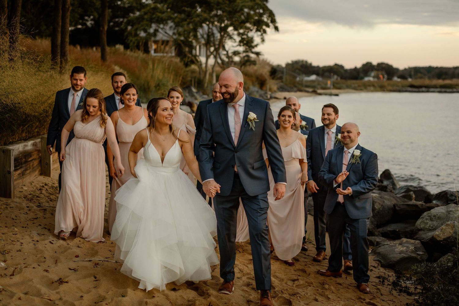 Wedding party walking along waterfront path with scenic coastal views.