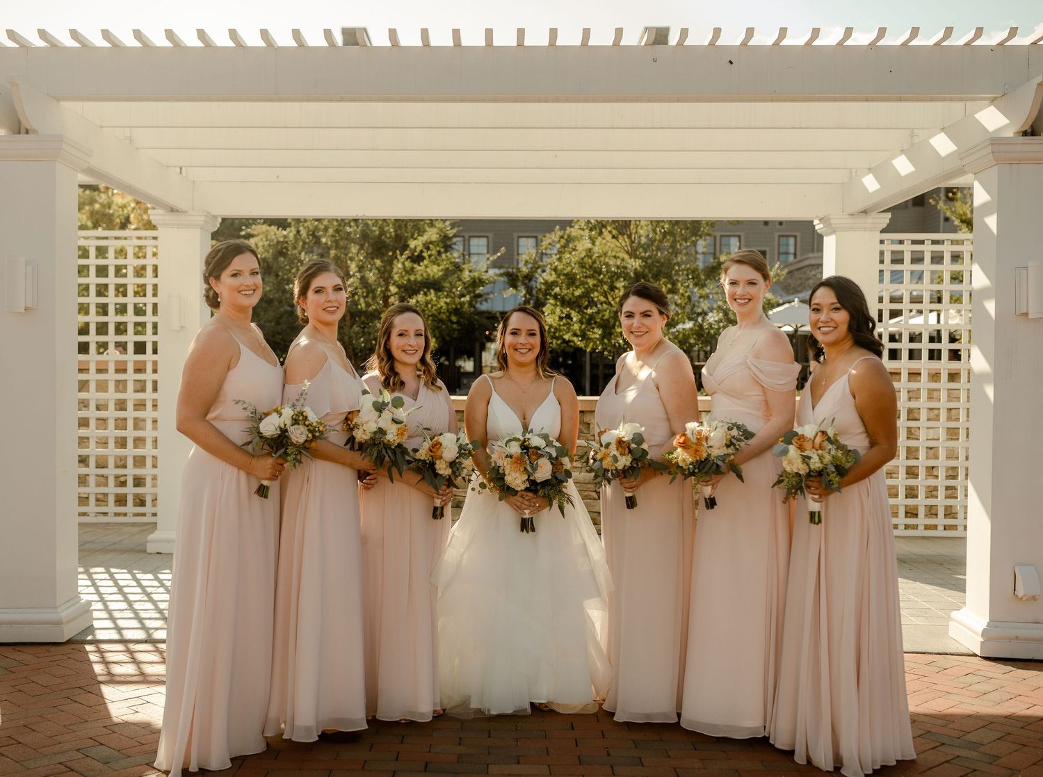 Wedding party lined up under white pergola with floral decorations and lattice details.