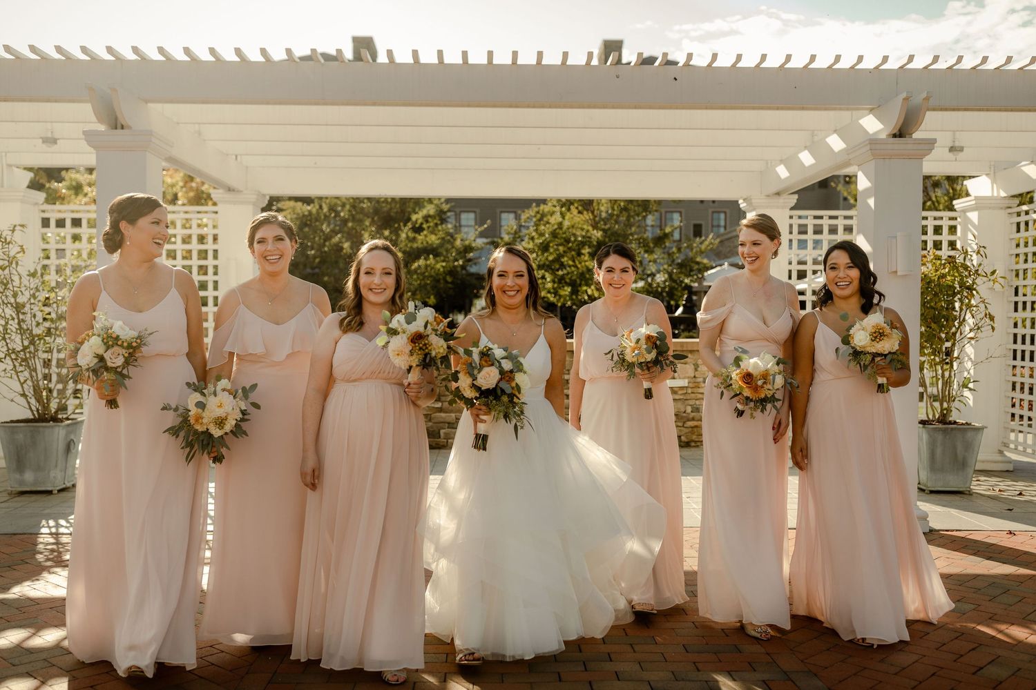 Wedding party posing under white lattice pergola decorated with floral arrangements.