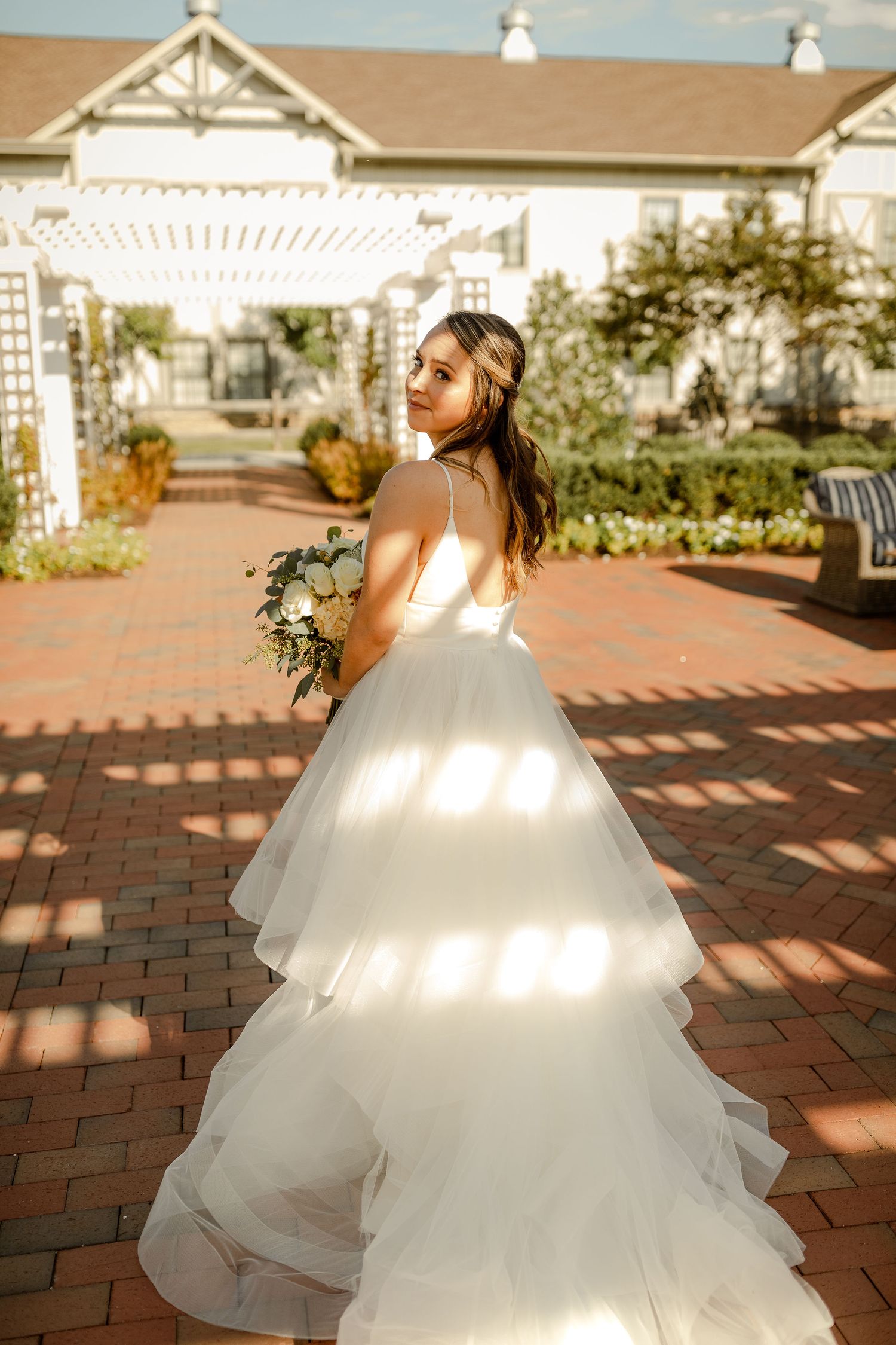 Flowing white wedding gown captured in sunlight on brick courtyard.