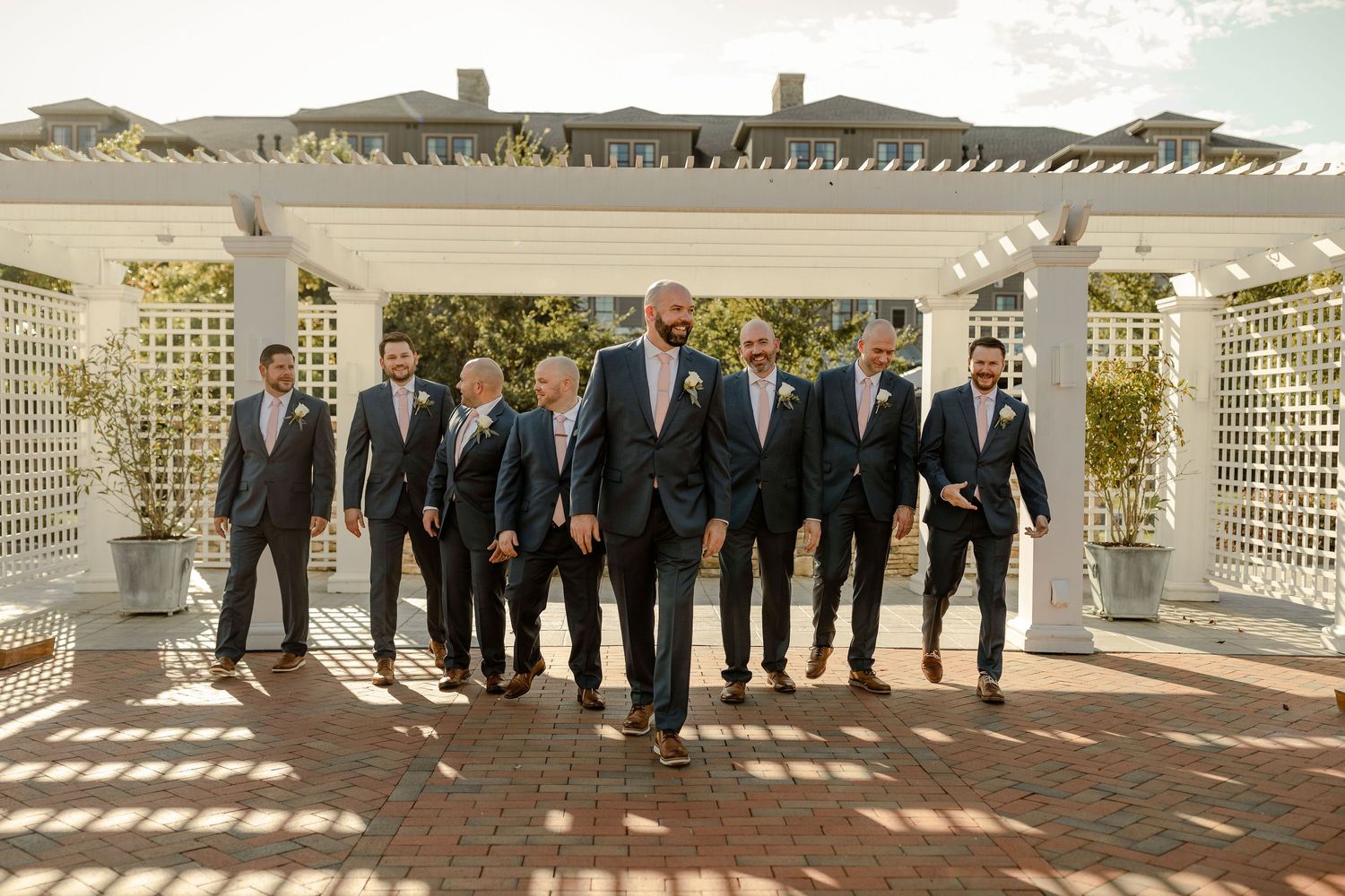 Wedding party in navy suits standing in formation on white lattice patio overlooking waterfront.