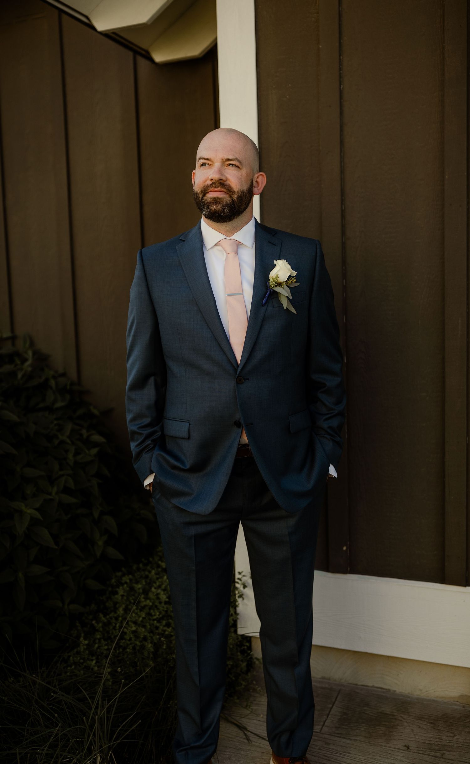 Groomsmen in navy suits and light pink ties posing against dark wood paneled wall.