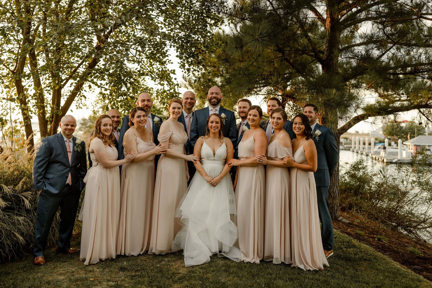 Wedding party in blush and navy poses under tall pine trees at outdoor venue.