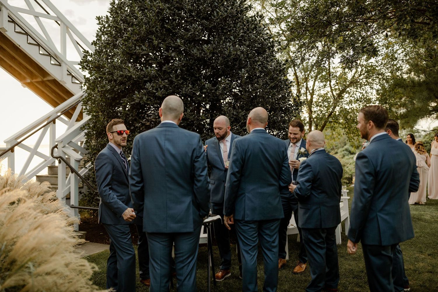 Groomsmen in navy suits gathered on scenic outdoor path surrounded by greenery.