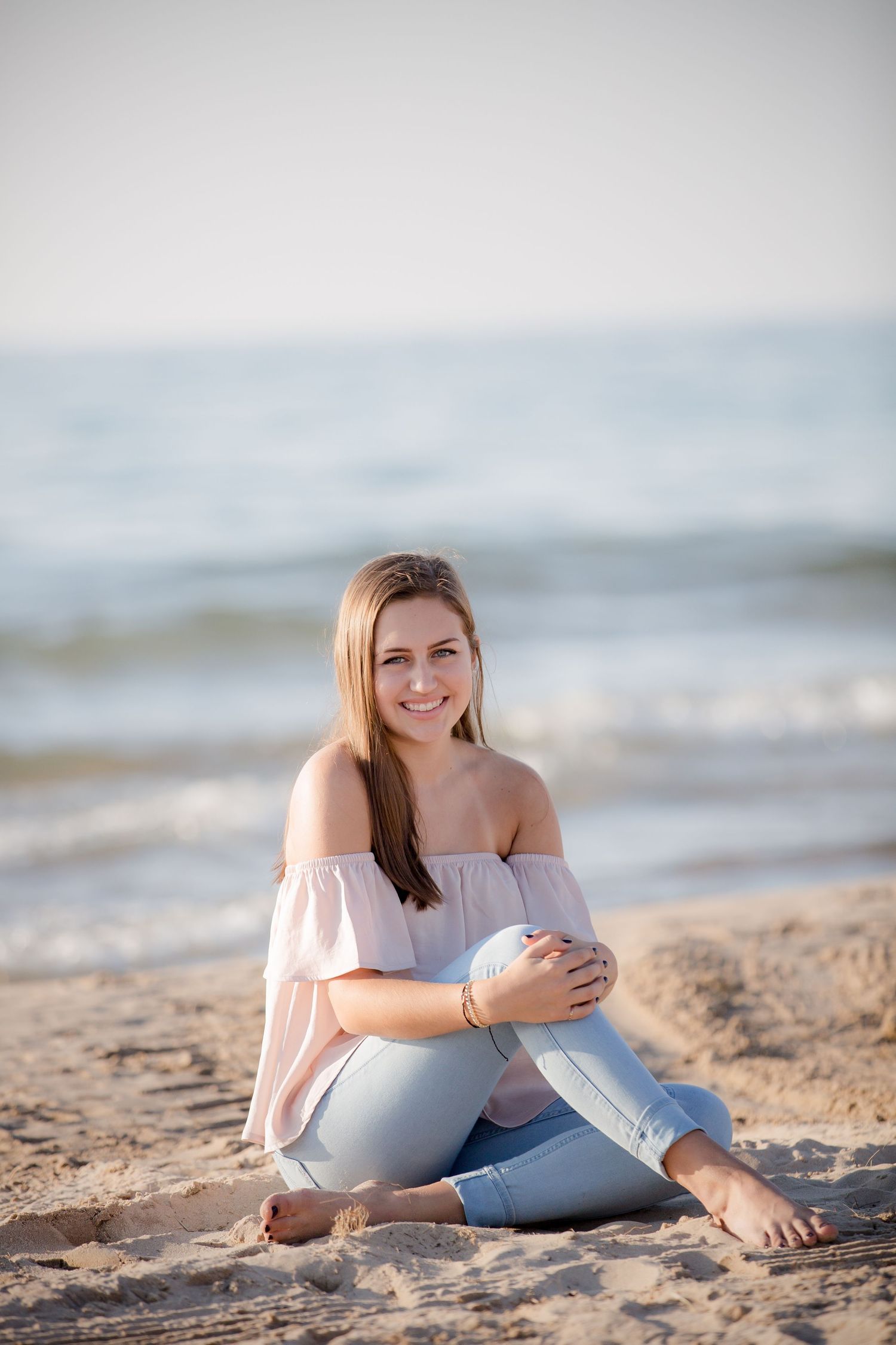 Young woman in off-shoulder top relaxing on sandy beach at sunset.