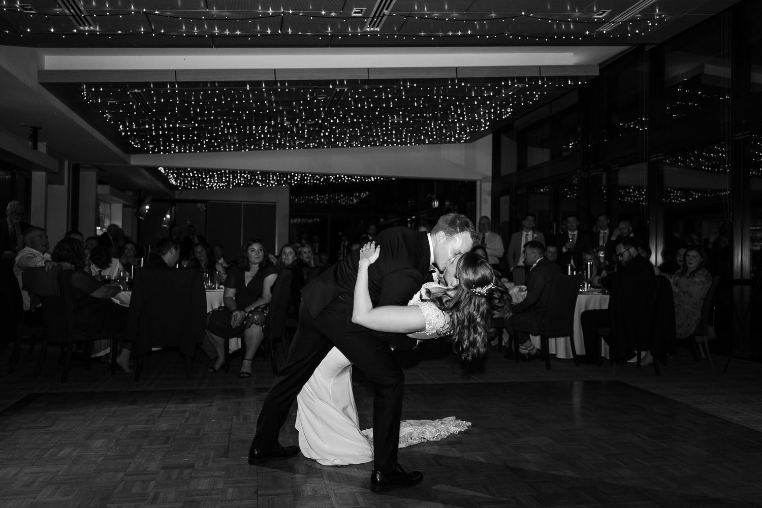 Wedding reception first dance in dark ballroom with guests watching.