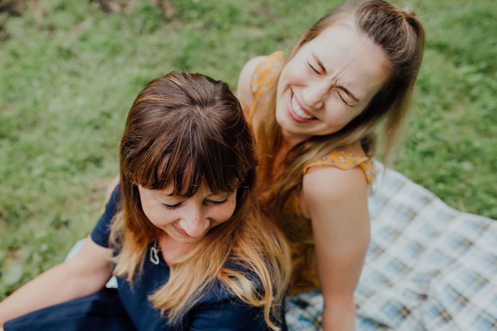 Zwei Personen lachen zusammen, während sie auf einer Picknickdecke im Freien auf dem grünen Gras sitzen.