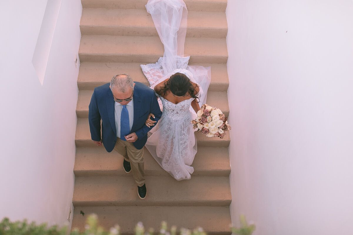A couple in wedding attire descending outdoor pink stairs together as seen from above.On Κτημα 48 captured by GeorgeNafpliotis.com