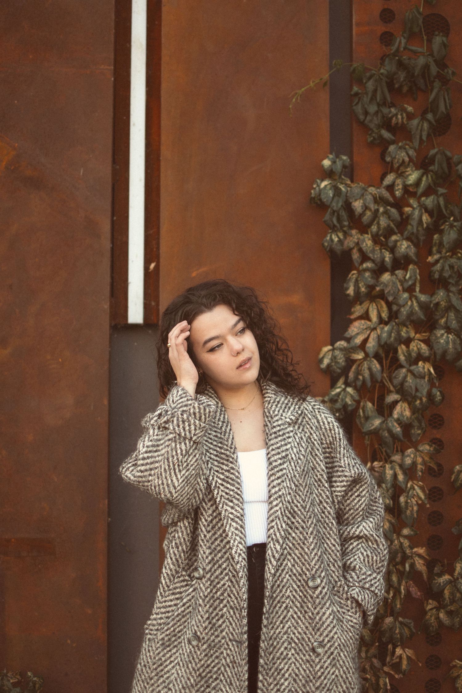 A moody portrait against a rust-colored wall showing a herringbone coat and natural curls.
