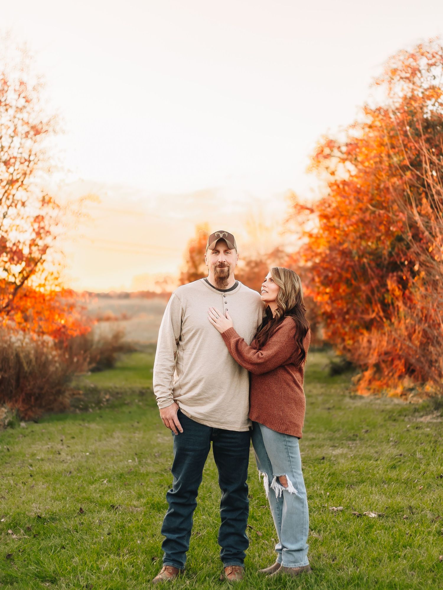 Couple taking casual outdoor portraits in a field during golden hour autumn light.