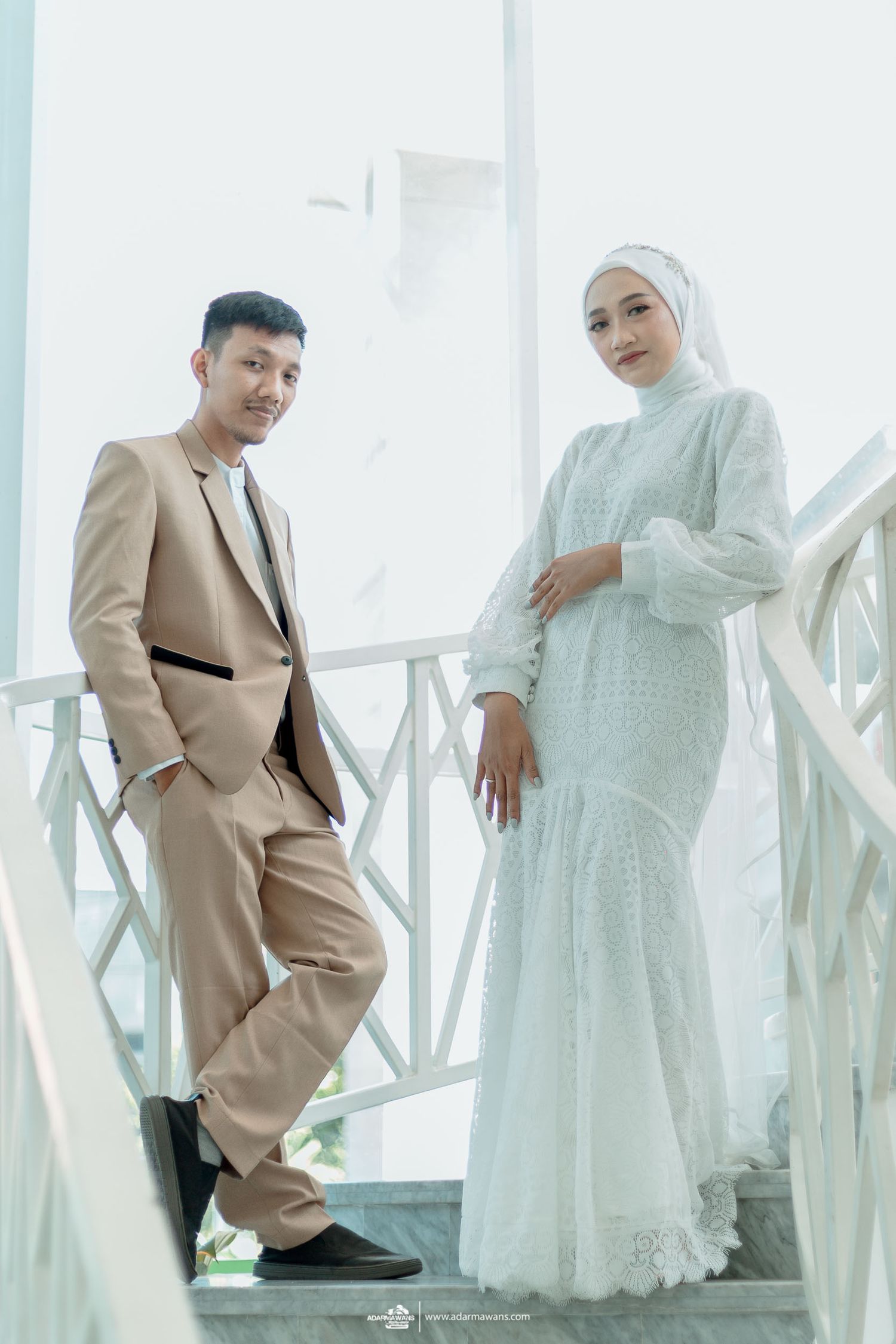 Couple poses on white modern staircase in complementary beige and white formal attire.
