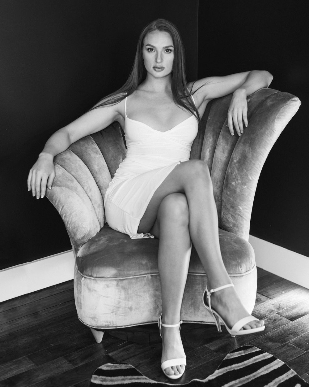 Black and white portrait on plush velvet chair showing classic glamour pose.