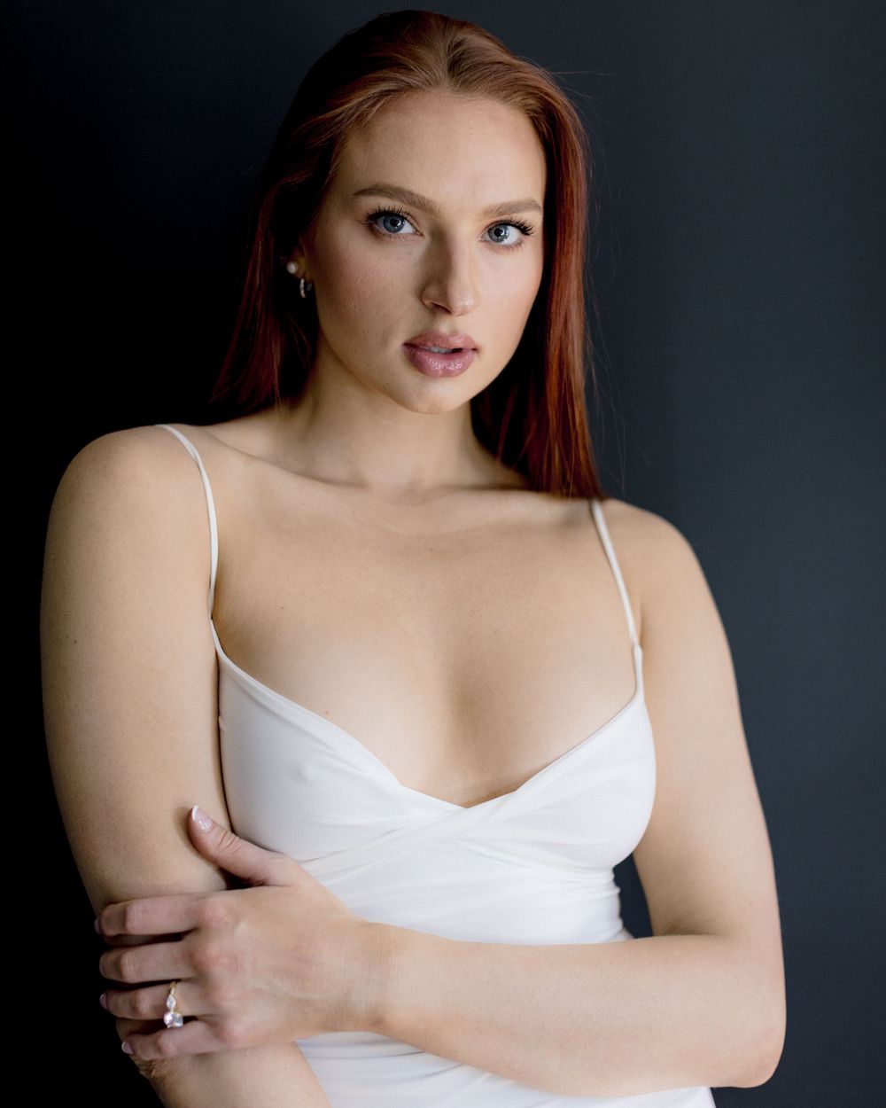 Portrait against dark background wearing white spaghetti strap top with elegant styling and dramatic lighting.