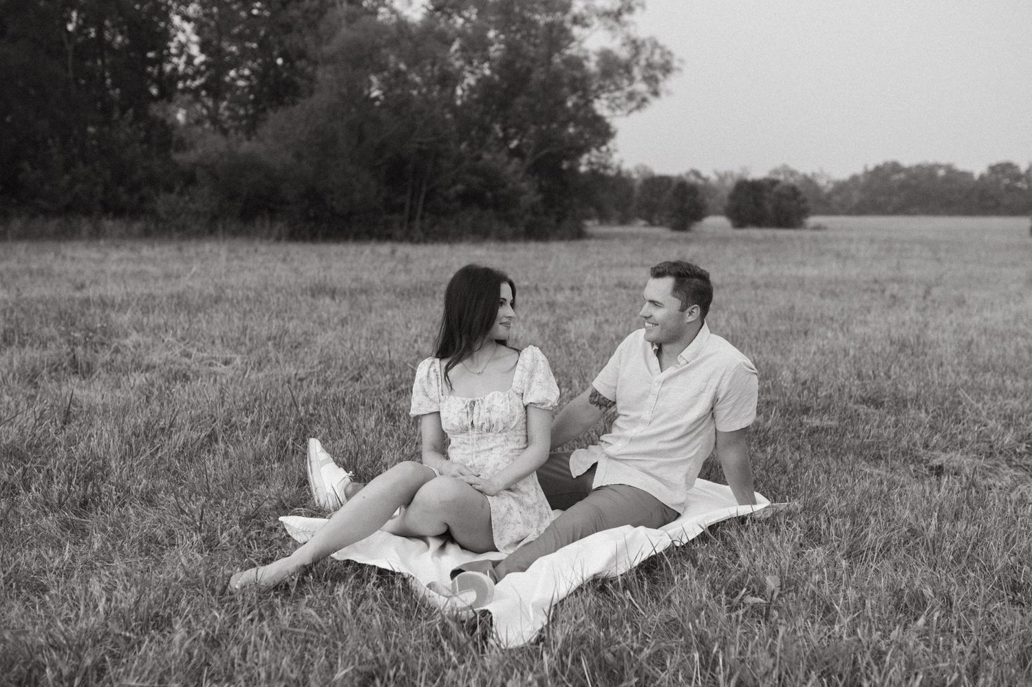 A romantic picnic scene in a grassy field with a white blanket laid out on the ground.