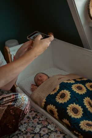 moeder neemt een foto op haar telefoon van haar baby die slaapt in de co-sleeper