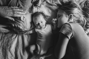 oudere broer en zus liggen op bed met baby broertje