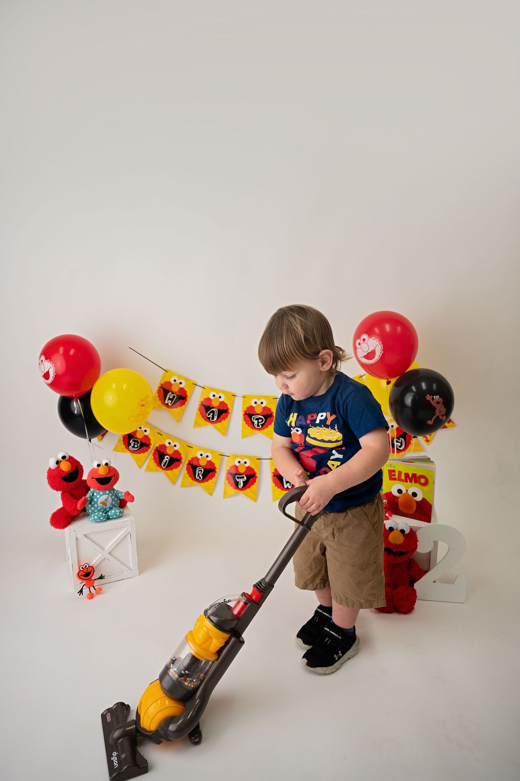 A child using a toy vacuum cleaner with Sesame Street themed party decorations in the background.