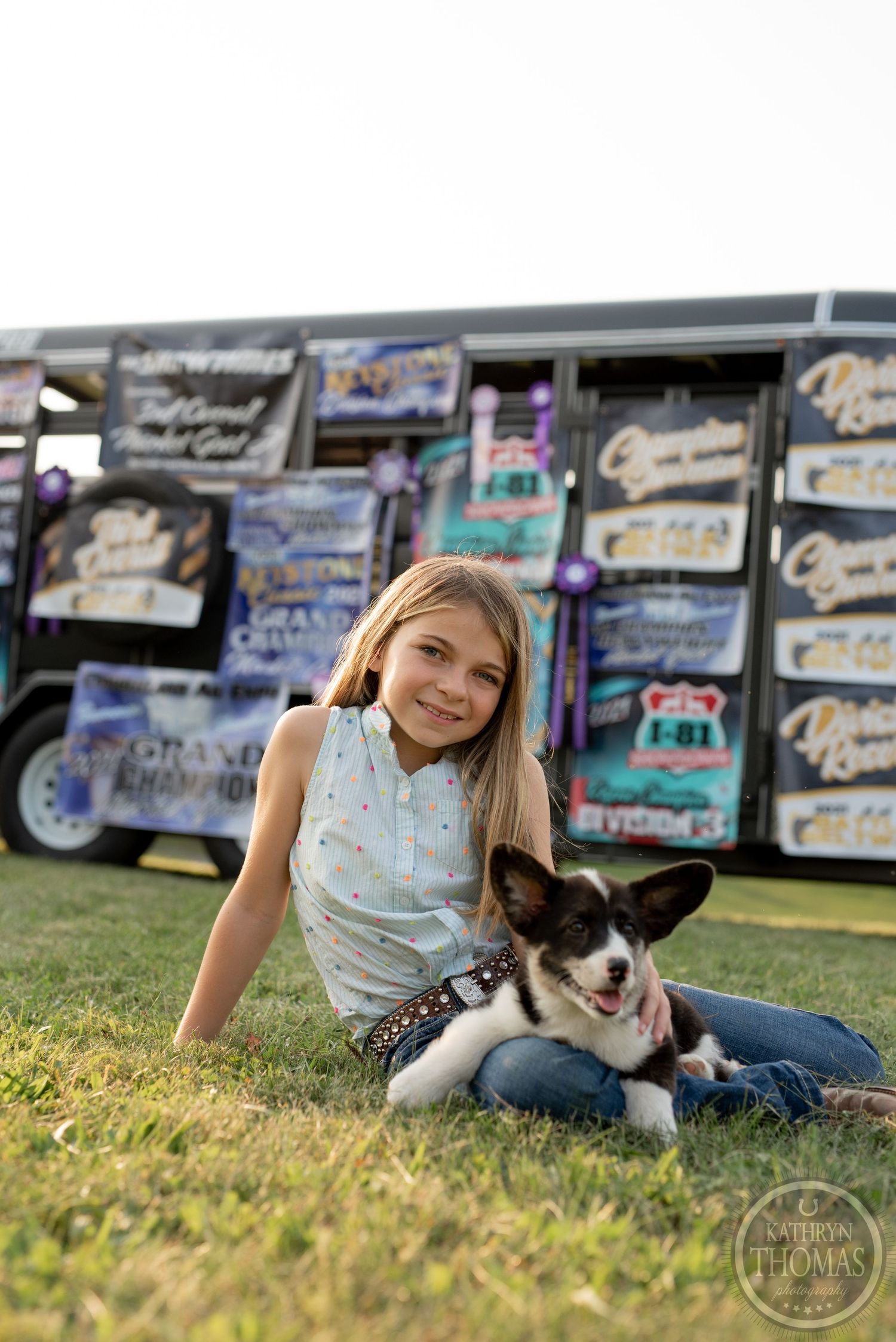 Person cuddles with black and white dog on grass near display of show banners.