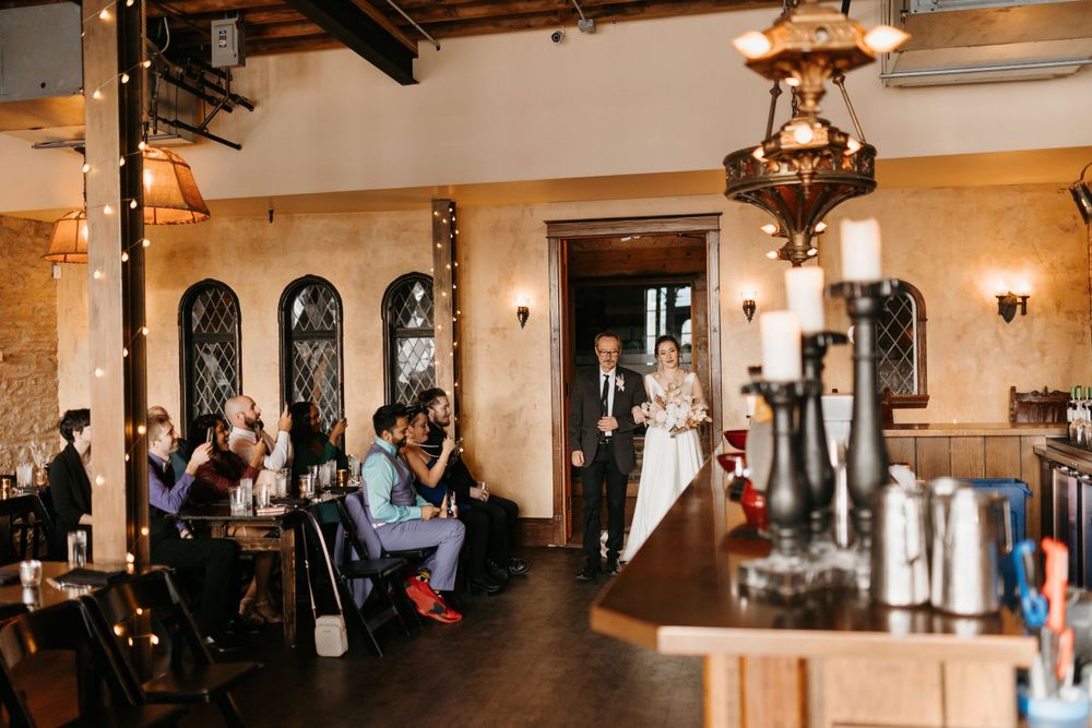 Wide shot of indoor wedding ceremony in rustic venue with exposed brick walls and arched windows.
