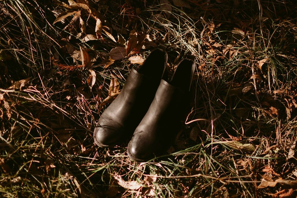 Black leather boots rest among fallen autumn leaves and dried grass.