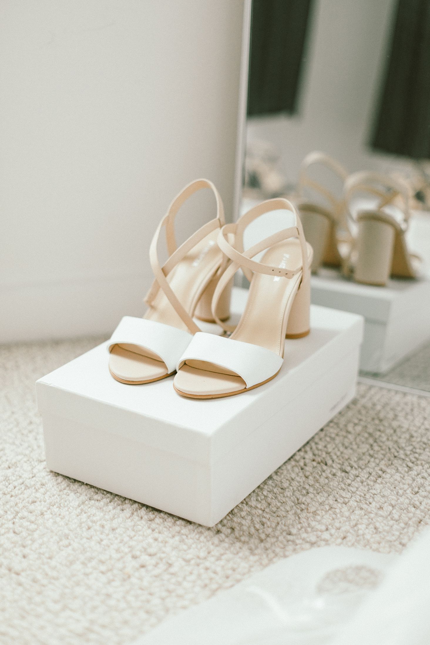 Elegant white strappy bridal sandals with nude accents displayed on a white pedestal.