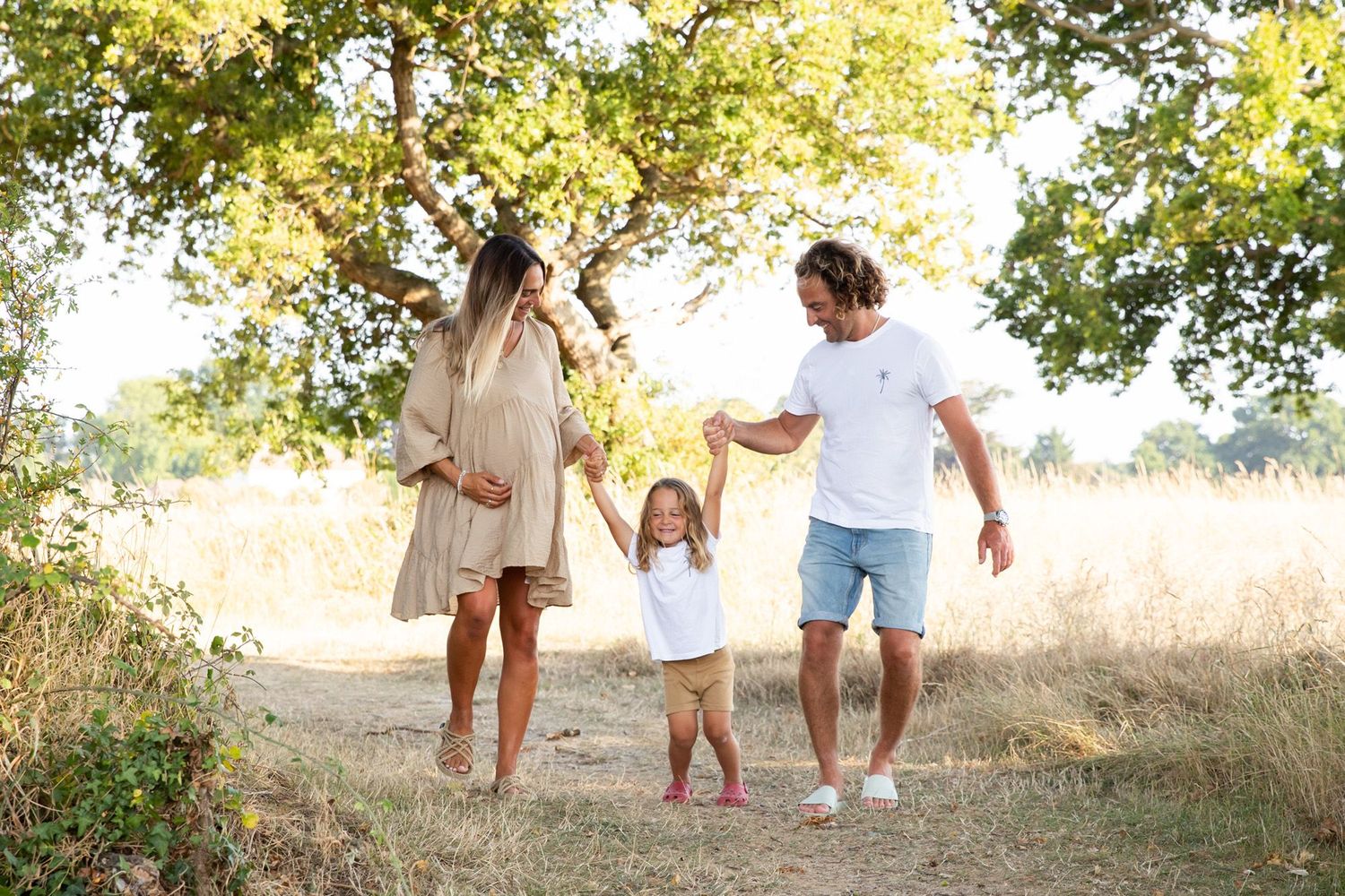 A family holding hands and playing together in a sunlit field with tall grass.