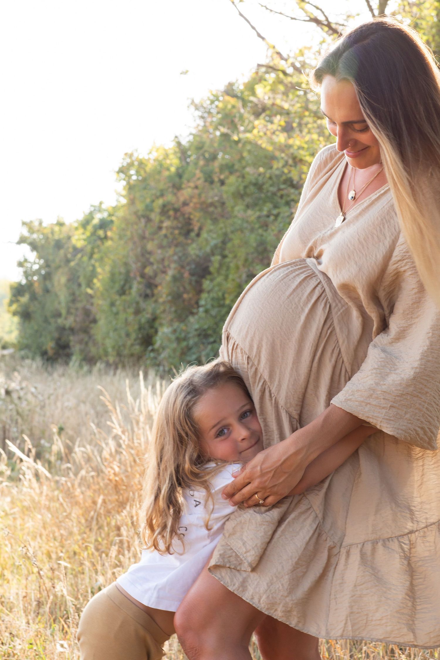 A tender moment between parent and child in golden sunlight against natural foliage.