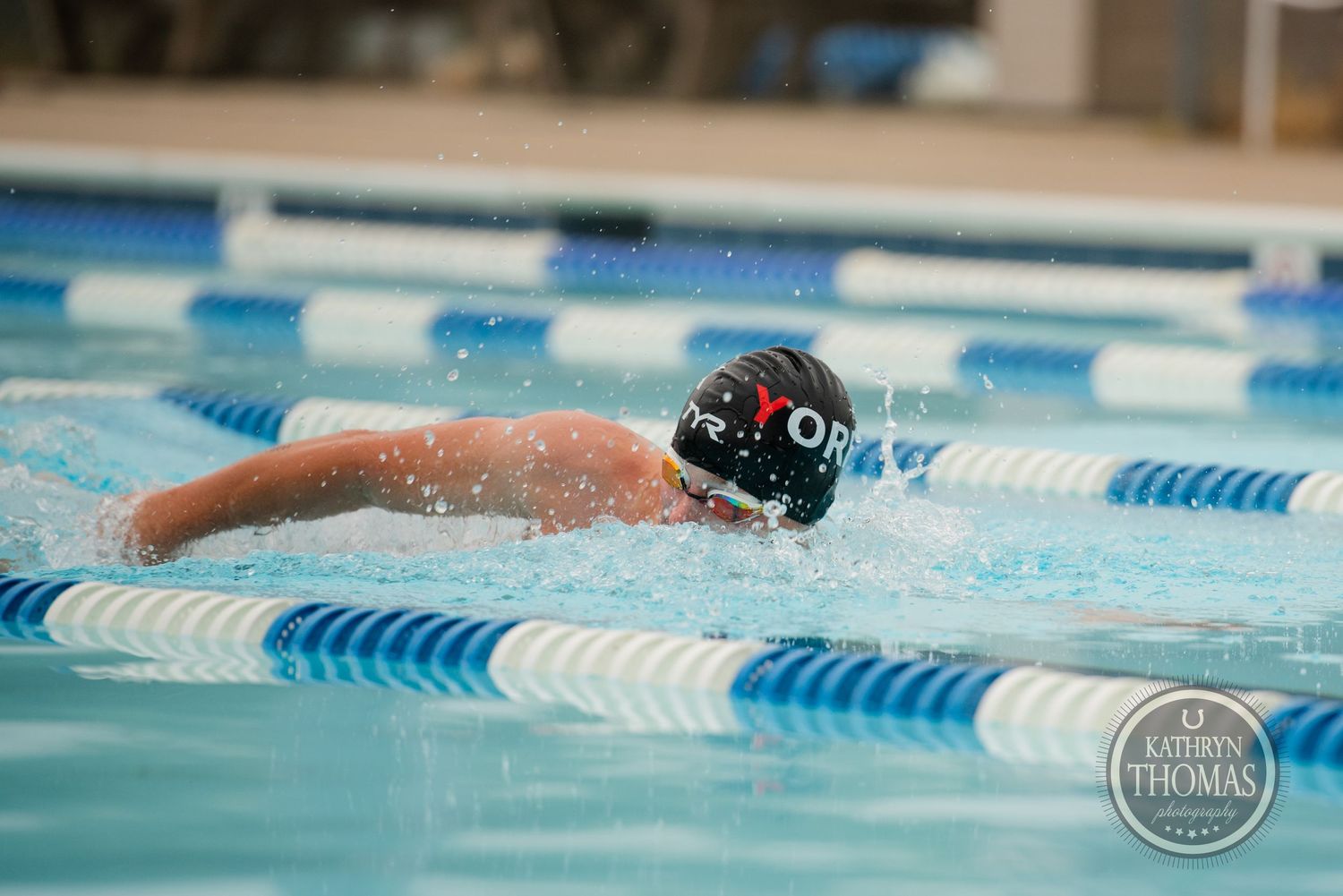 A swimmer performs freestyle stroke in a pool with blue lane dividers.