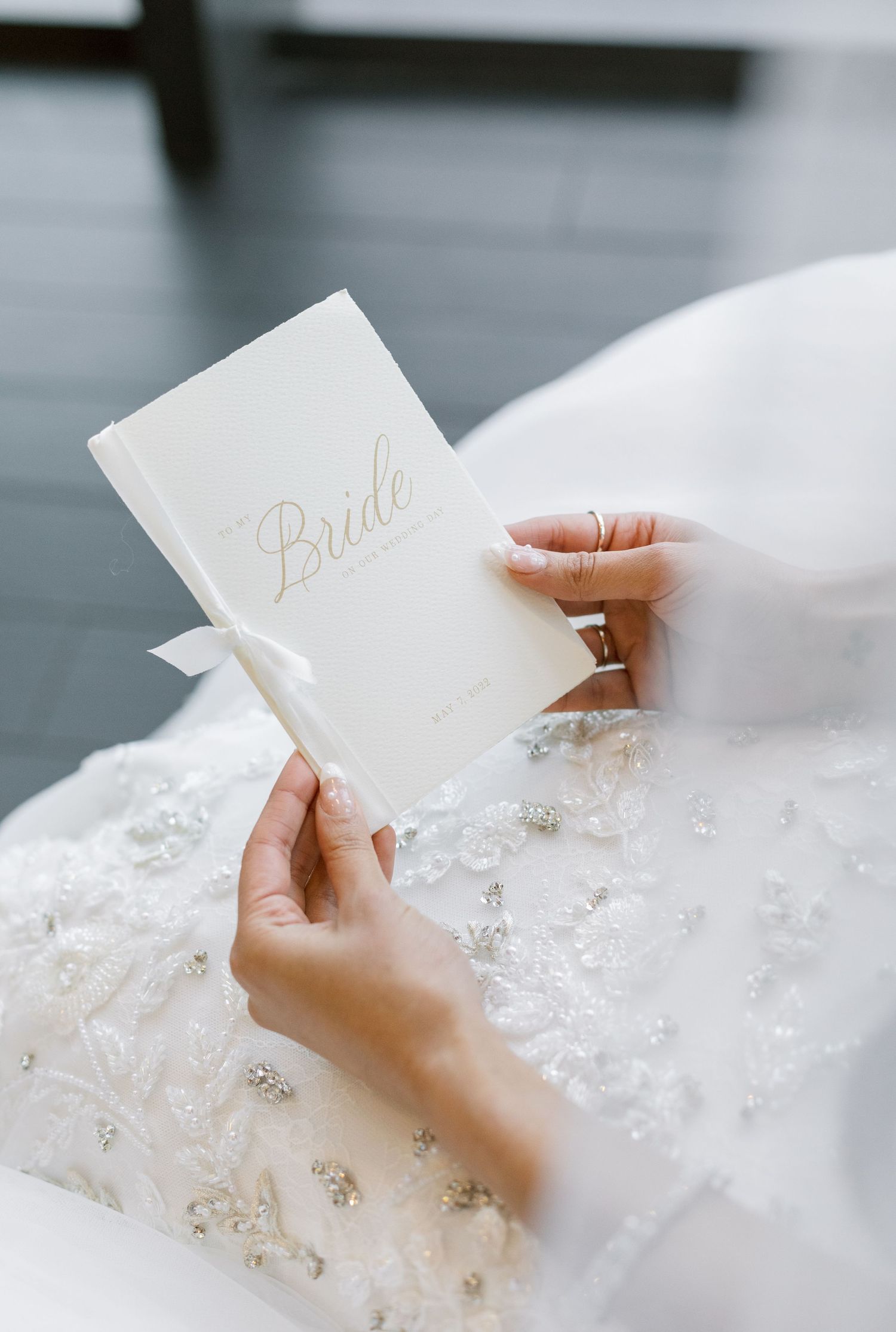 Hands holding an elegant white 'Bride' booklet against a lace dress.