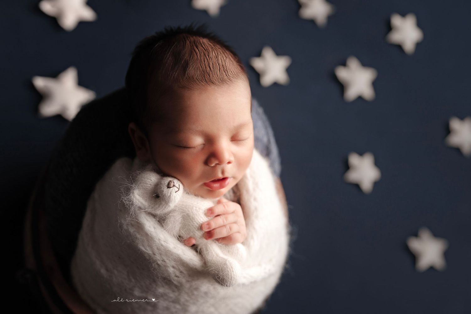 Newborn swaddled in white wrap against dark backdrop decorated with white stars.