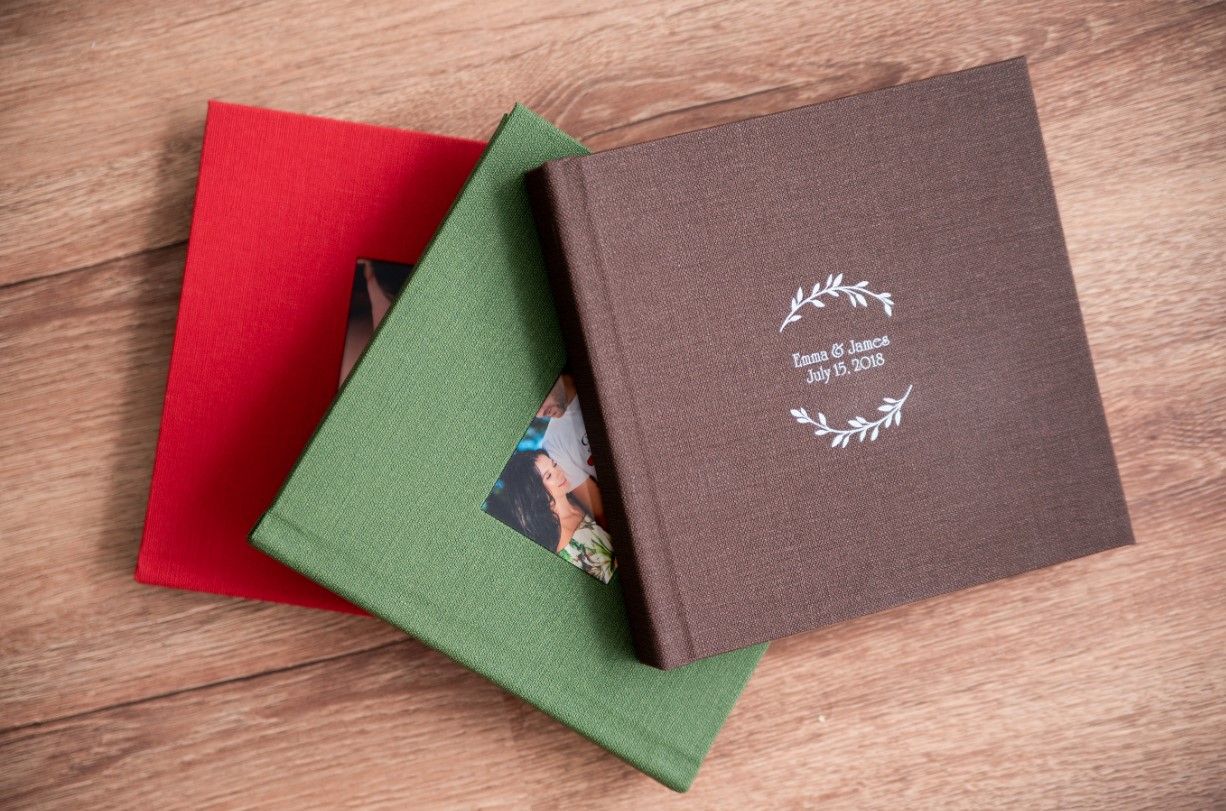 Brown and red photo albums arranged on wooden surface with colored envelopes.