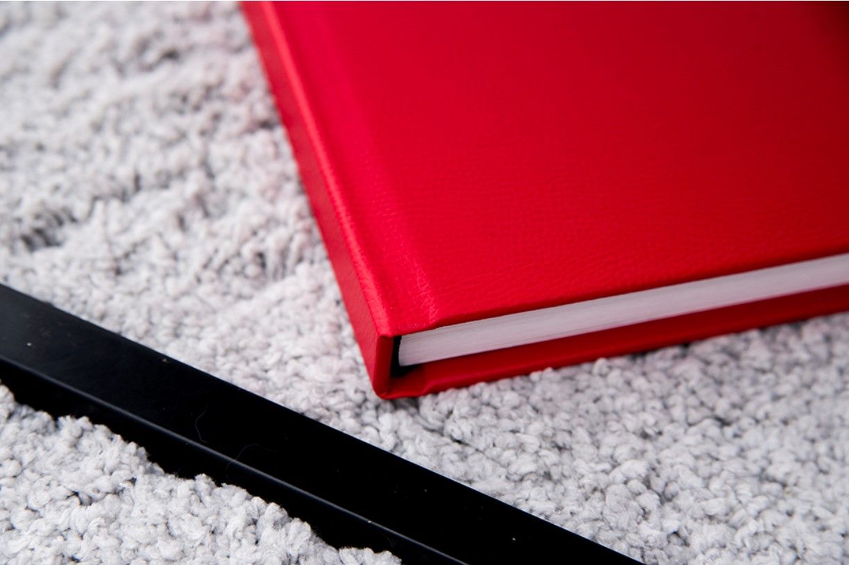 Red photo album lying on textured gray surface with dramatic lighting.