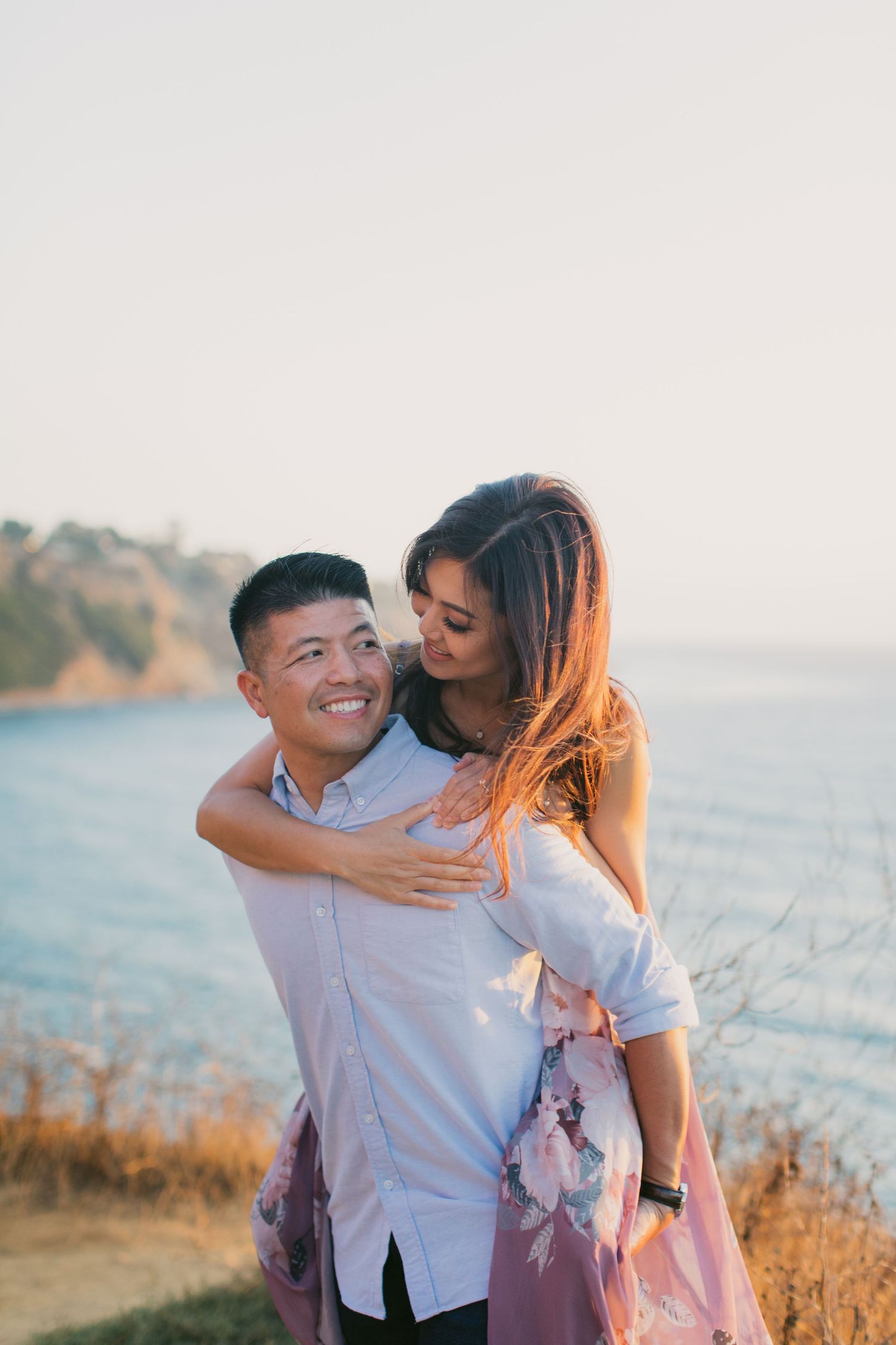 Playful couple sharing intimate moments during a sunset photoshoot by the ocean.