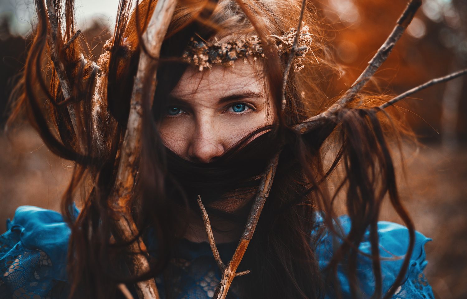 An ethereal portrait in autumn colors features a figure in blue with a delicate floral crown amid swirling branches.