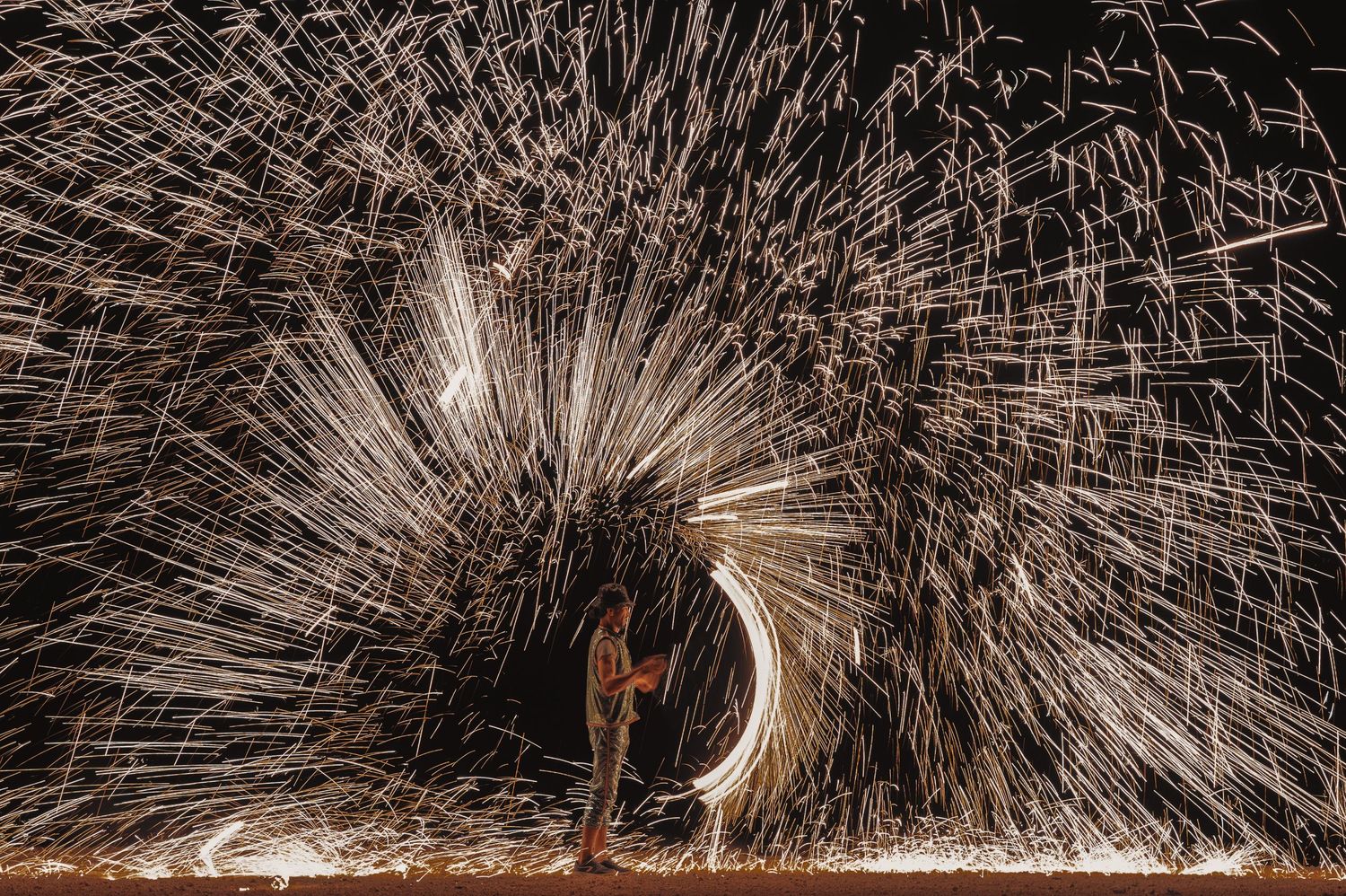 Dramatic long exposure shot of spinning steel wool creating light trails and sparks in the dark.