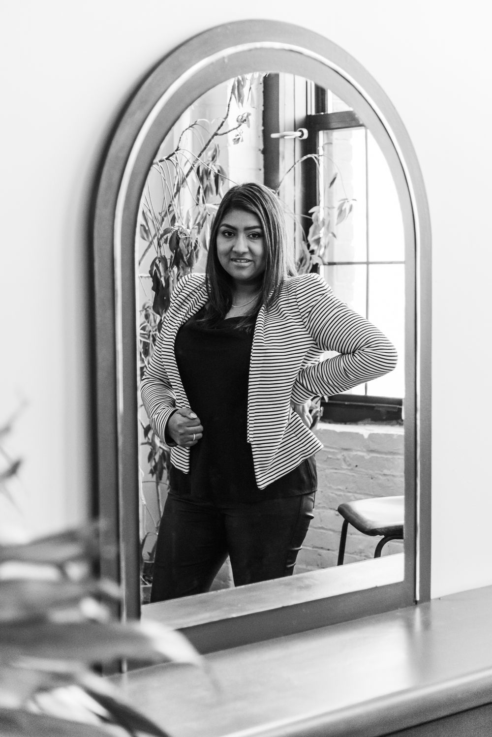 Black and white portrait of woman in striped blazer reflected in arched mirror.