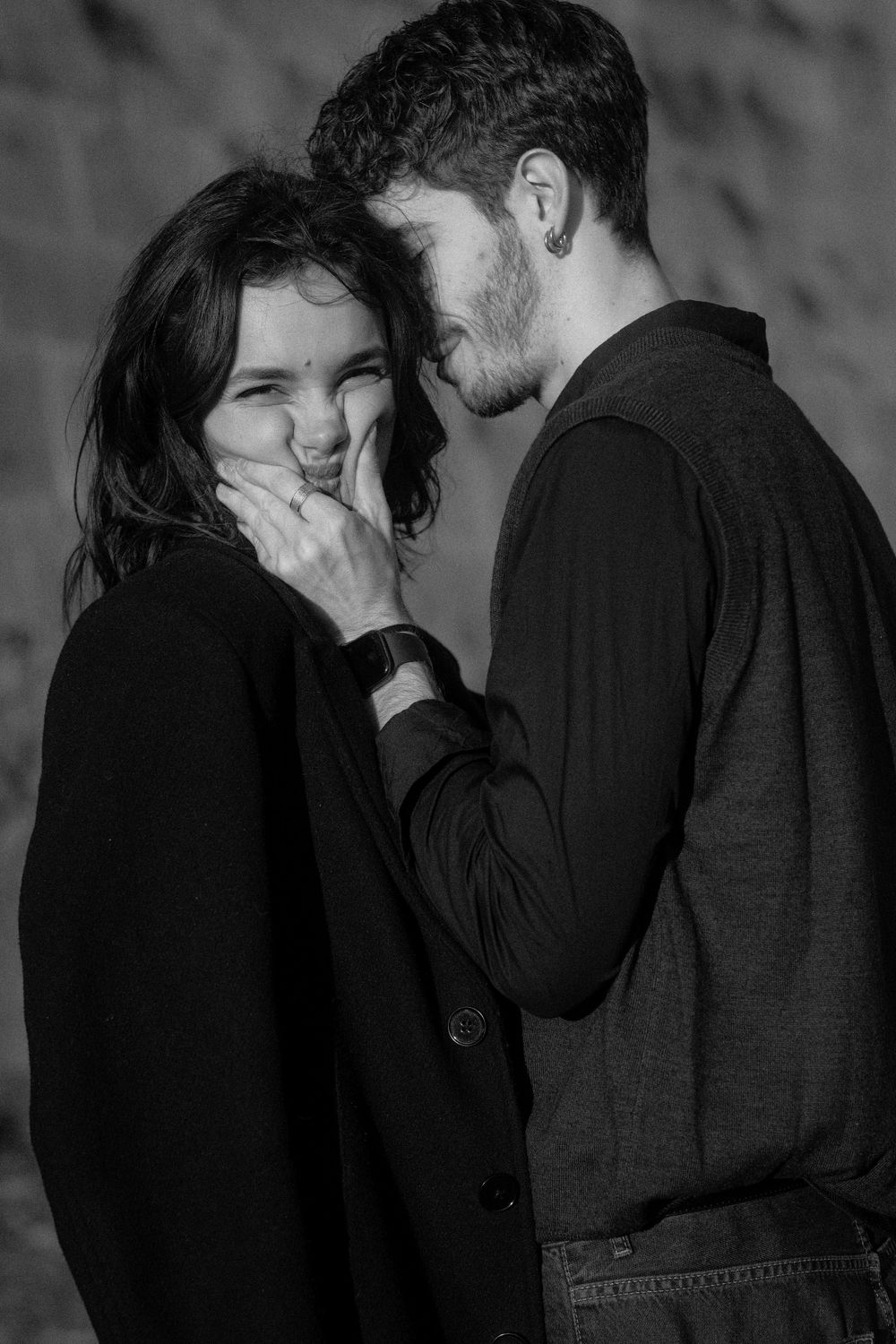 A romantic black and white photo capturing a playful moment between a couple in dark clothing.
