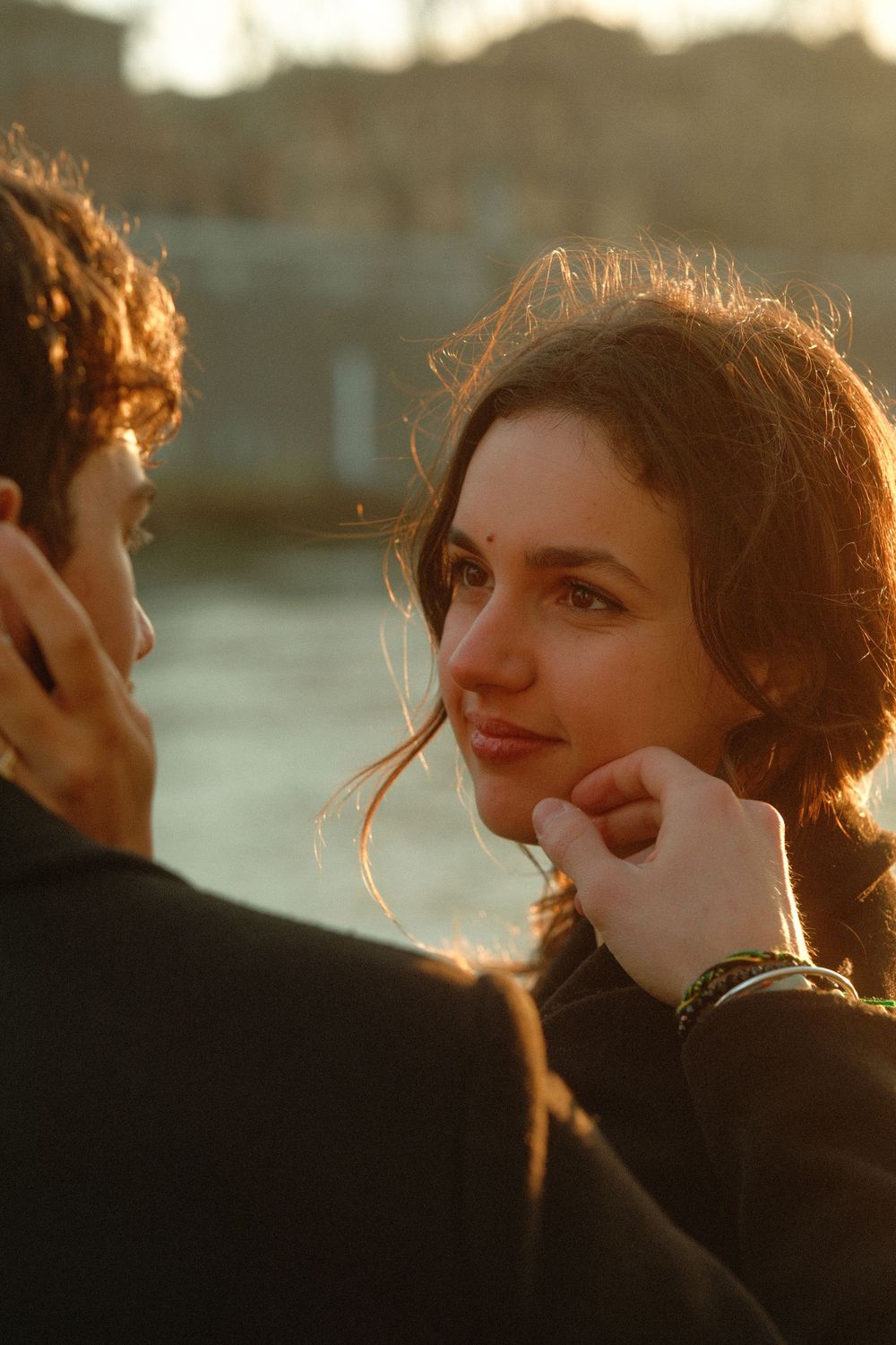 A romantic sunset portrait showing a tender moment between a couple in dark clothing.