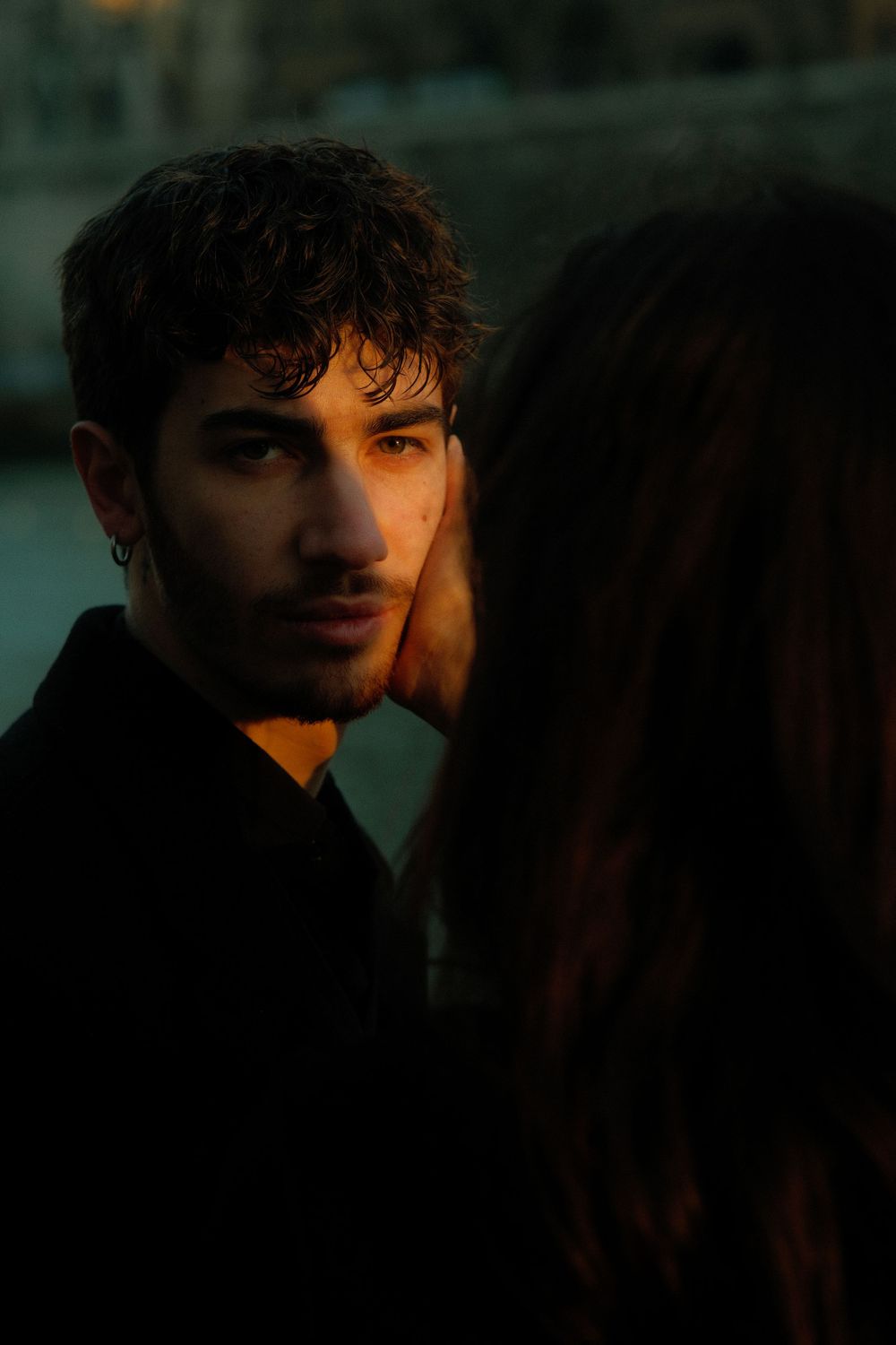 A moody portrait in low light showing a couple's intimate interaction at dusk.
