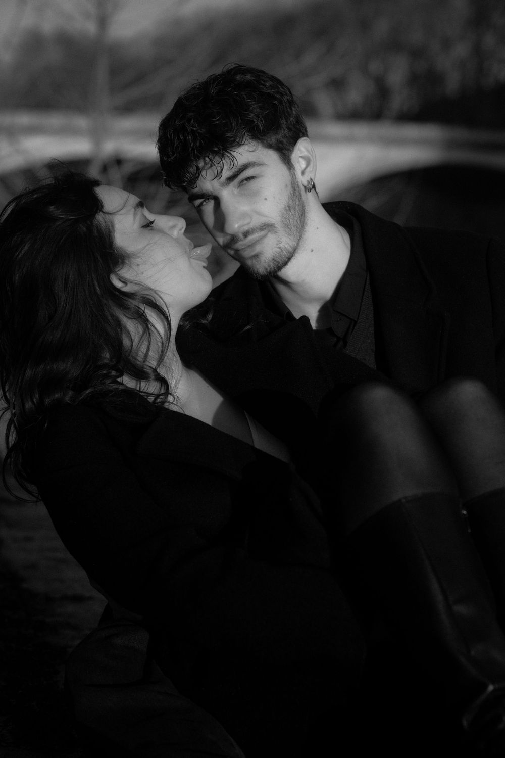 A moody black and white portrait of a couple in an intimate embrace during twilight.