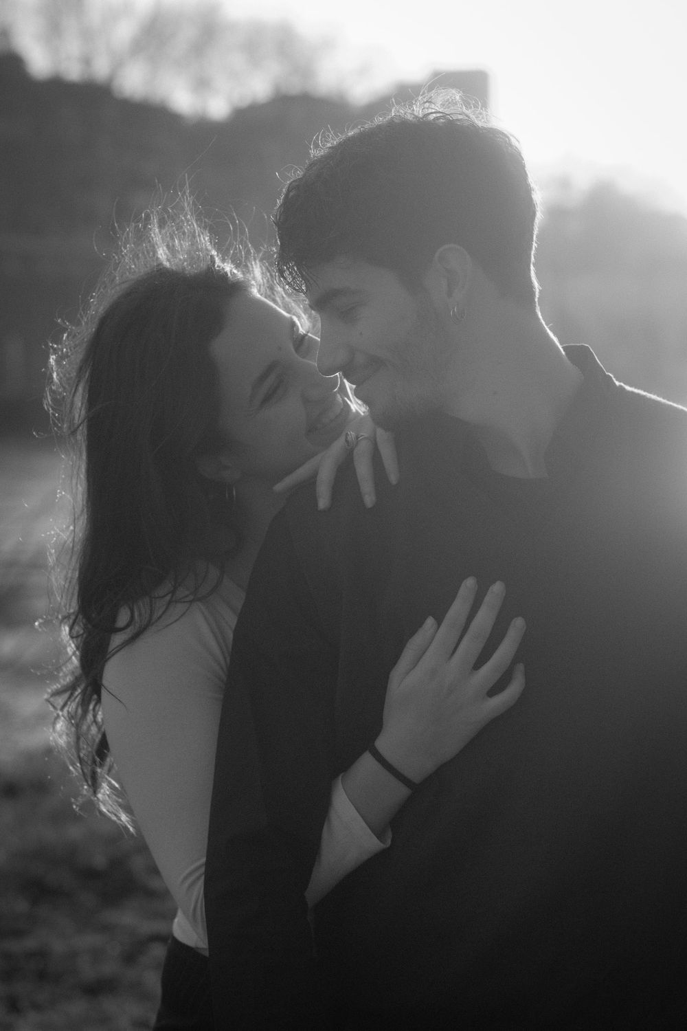 An intimate black and white portrait of a couple sharing a tender moment in natural backlight.