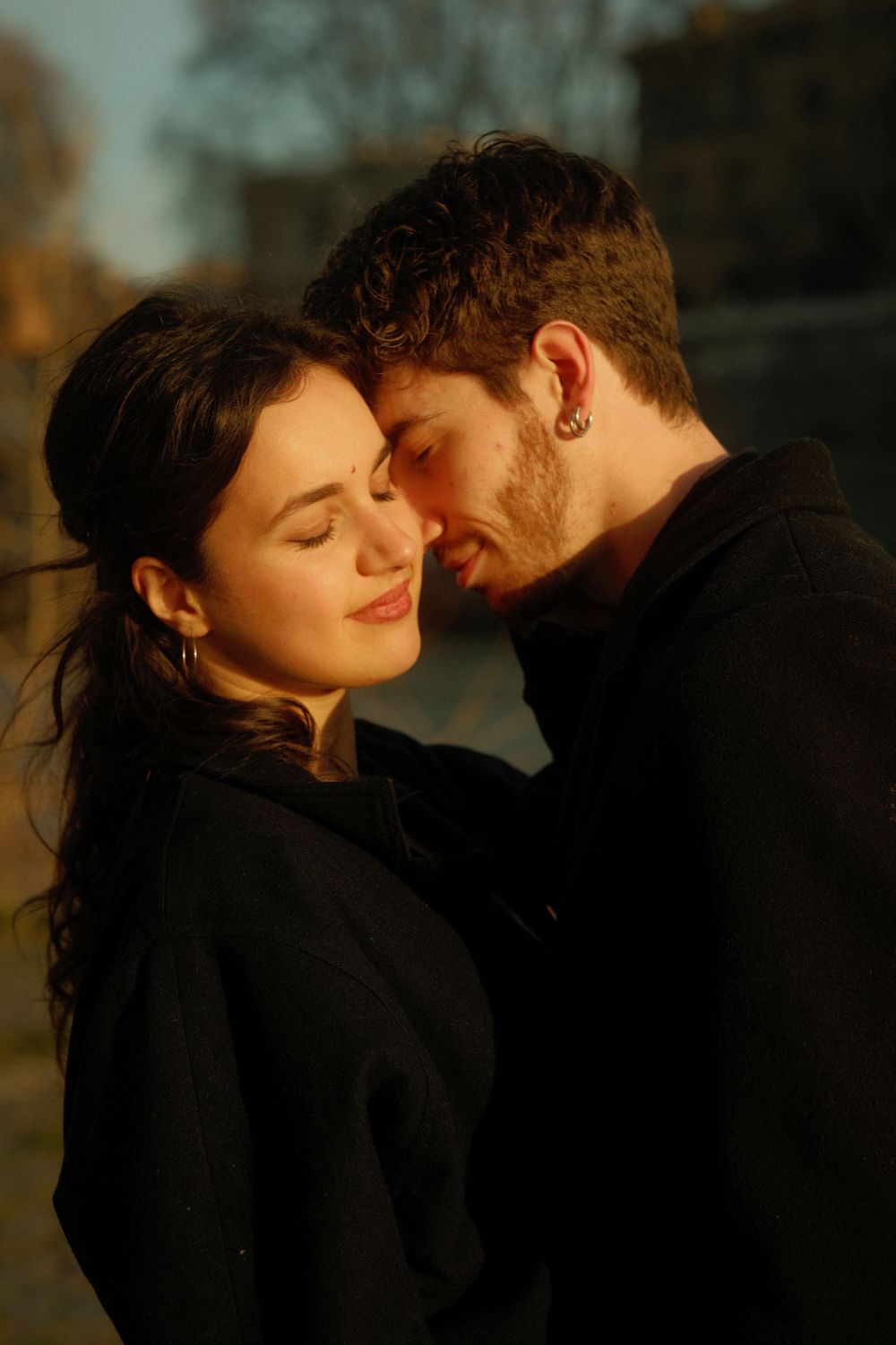 A tender sunset moment between a couple in black coats against a warm glowing background.