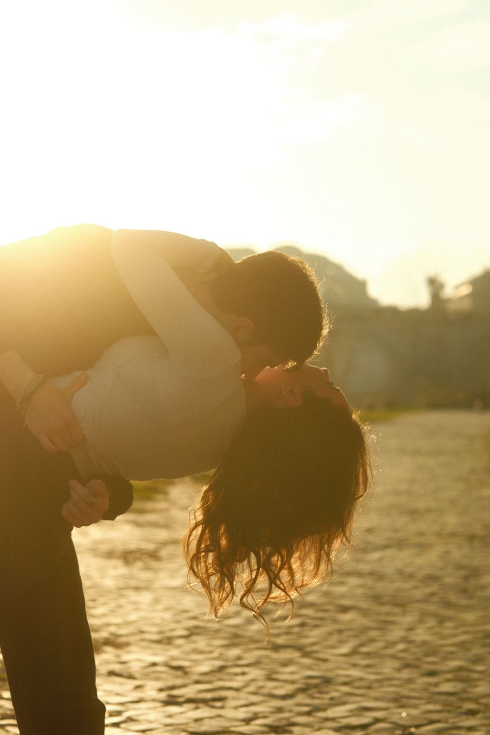 A silhouetted couple sharing a romantic dip pose against a golden sunset over water.