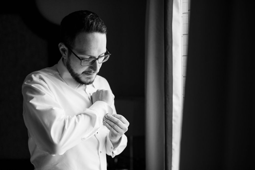 Black and white photo of person adjusting cuffs by window light.