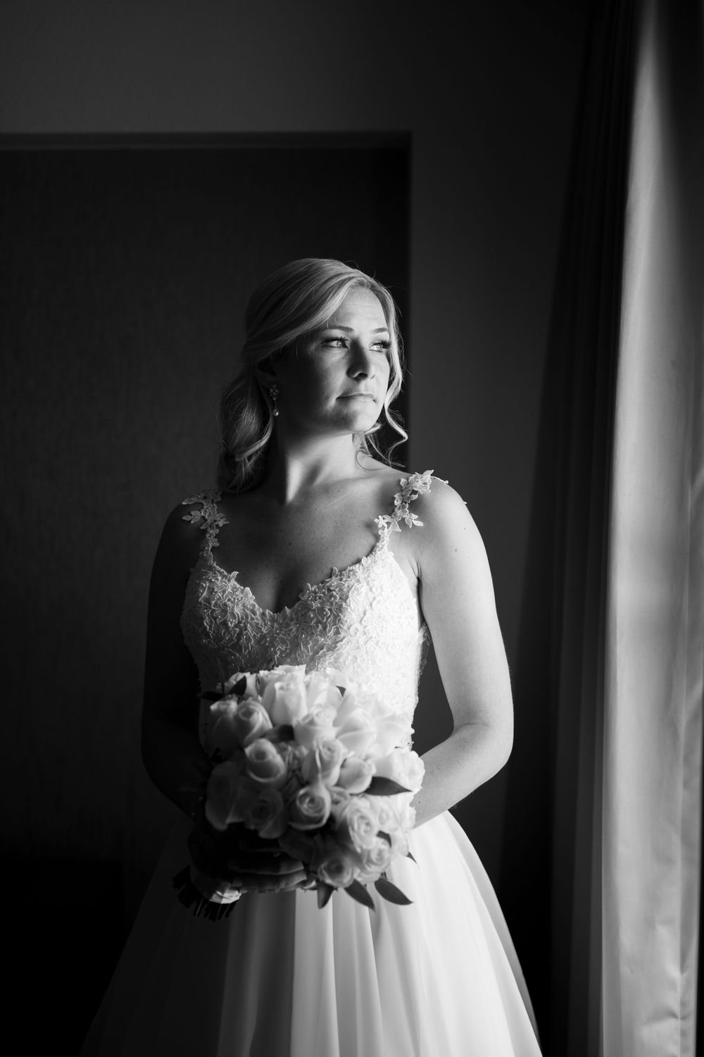 Black and white bridal portrait showing lace dress details and bouquet near window.