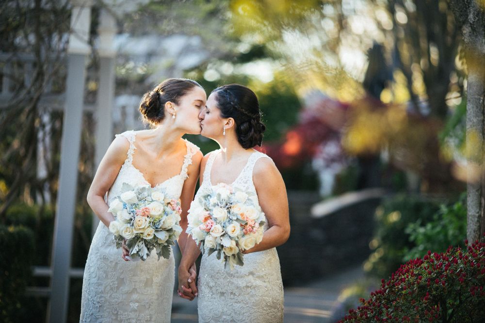 Brides share joyful moment together while holding matching white bouquets.