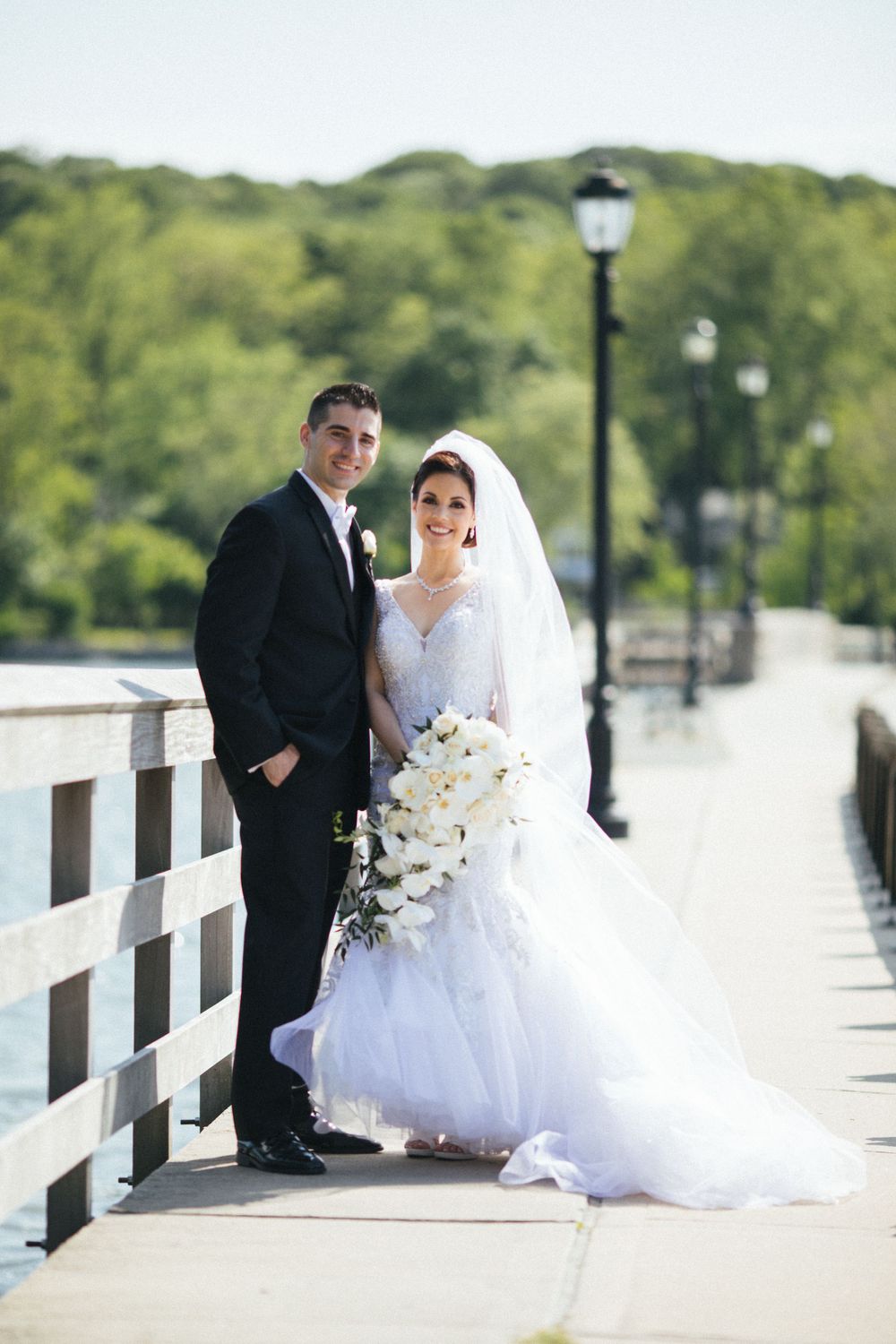 Elegant wedding portrait of couple posing on waterfront boardwalk with lamp posts.