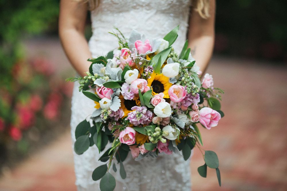 Close-up of bridal bouquet featuring pink roses, sunflowers and mixed garden flowers.
